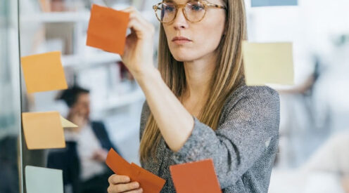 Female consultant arranging sticky notes on a glass wall during a metadata management consulting services session.
