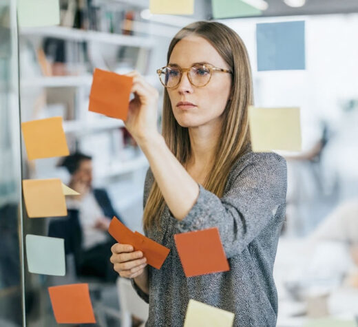 Female consultant arranging sticky notes on a glass wall during a metadata management consulting services session.